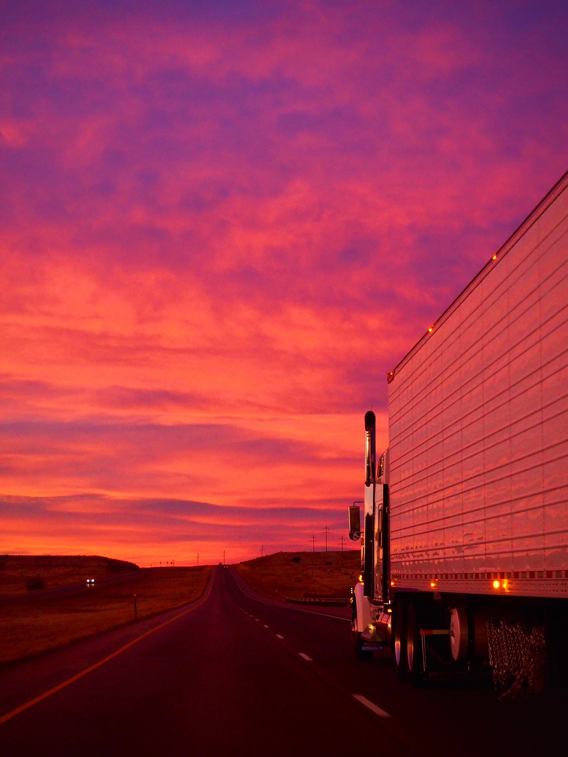 Semi Truck on the highway with a vibrant pink and purple sunset sky.